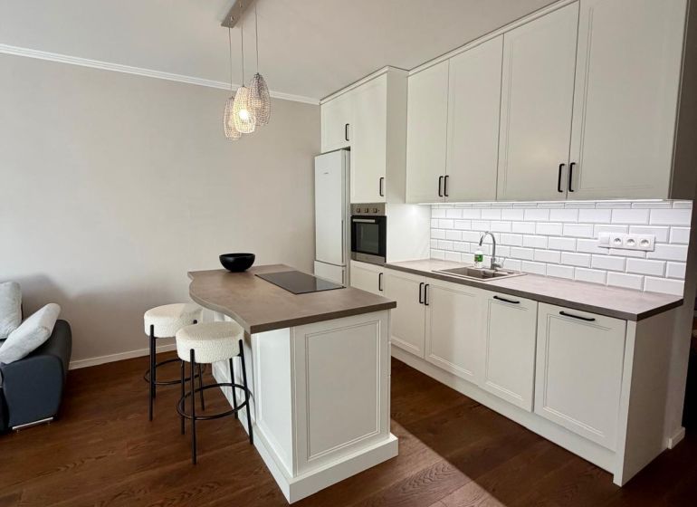 A kitchen in a 2-room apartment with an island, white cabinets, and a wood-patterned floor.