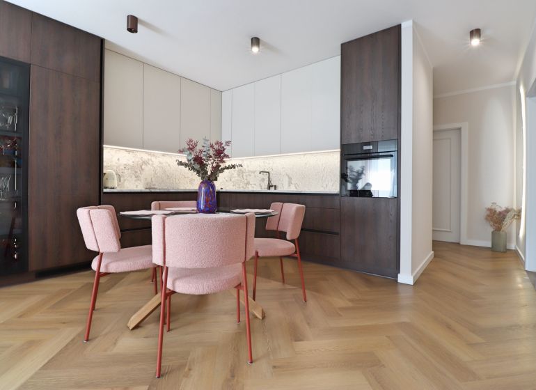 A kitchen in a 3-room apartment with a wood-patterned floor and pink chairs.