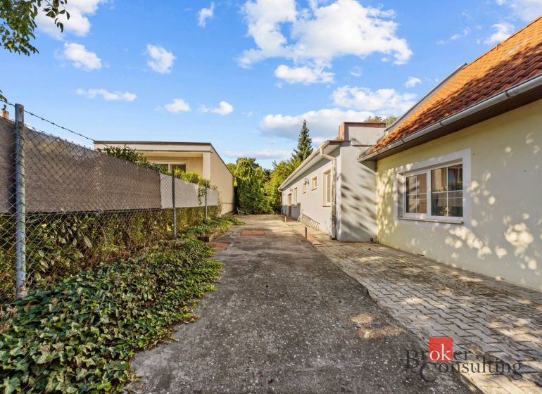 The exterior of a family house in Budmerice, a paved path surrounded by greenery and a fence.