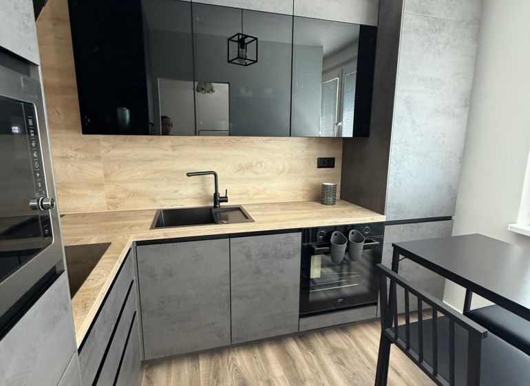 A kitchen with black and gray cabinets, a wood-patterned floor, and a dining table in a studio apartment.