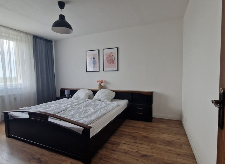 A bedroom in a two-room apartment with a wooden decor floor, a bed, and pictures on the wall.