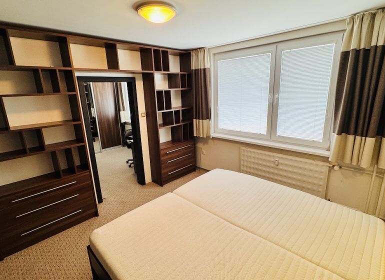A bedroom with shelves in a 3-room apartment, equipped with a large window with blinds.