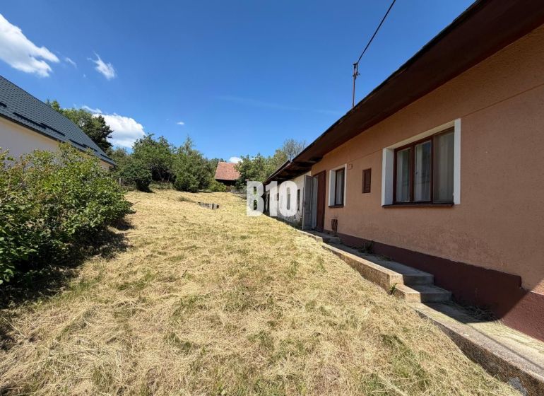 A cottage in Dubové with a garden and surrounding nature on a slope, blue sky.