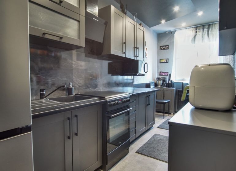 A kitchen in a 3-room apartment with gray cabinets and stainless steel appliances.