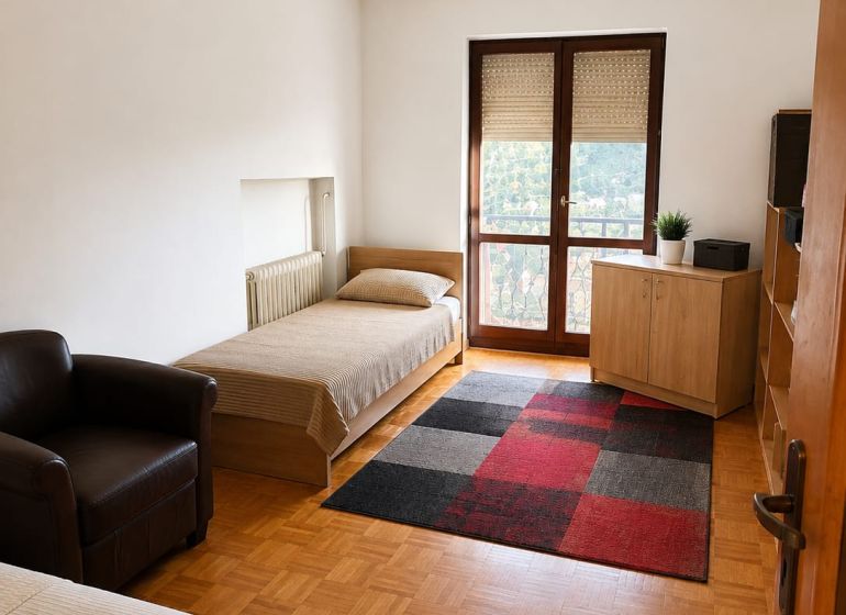 A room in a 3-room apartment with beds, a chair, a carpet, and a floor with a wooden decor.