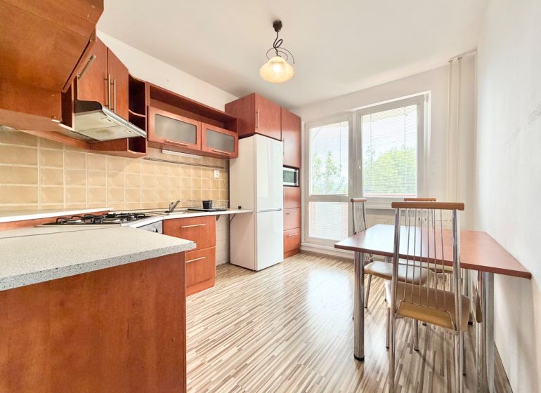 A kitchen in a 2-room apartment with a wooden decor floor, a dining table, and appliances.