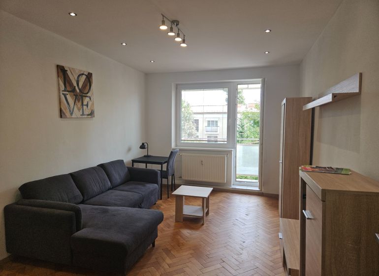 A comfortable living room with a sofa, a desk, and a wooden decor floor in a two-room apartment.