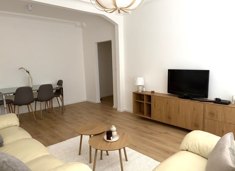 Living room of a three-room apartment with a wooden decor floor, a sofa, and a dining table.