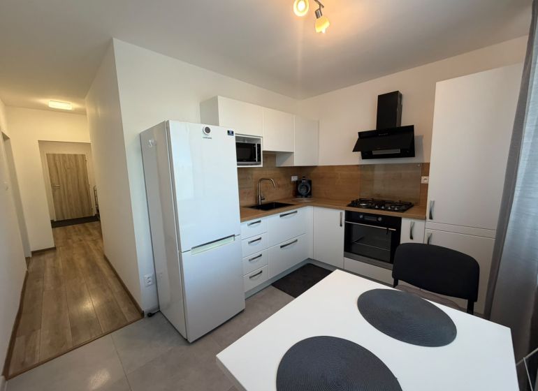 A kitchen in a 2-room apartment with a white kitchen unit and a floor with a wood decor.