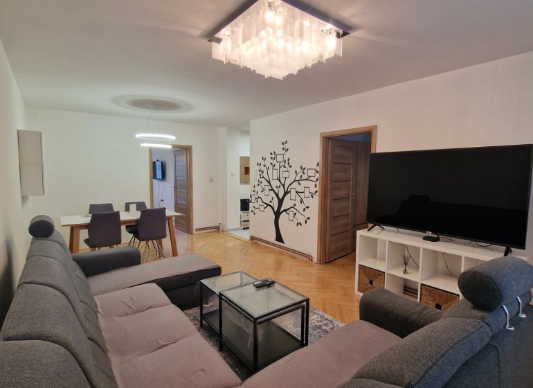 Living room with a large TV, gray sofa, and wooden decor flooring in a 3-room apartment.