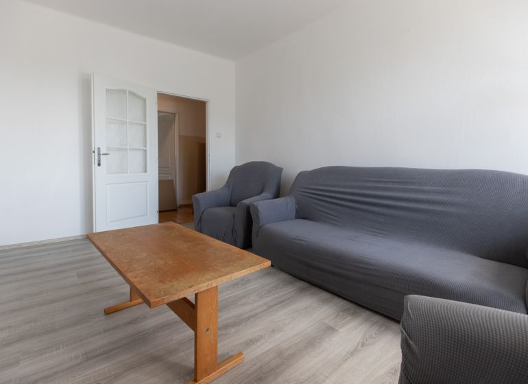 Living room with a sofa, an armchair, a wooden table, and a wooden-patterned floor in a 3-room apartment.