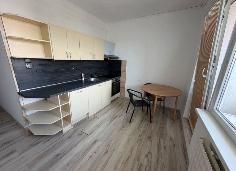 A kitchen in a 2-room apartment with a wooden decor floor and a dining area.