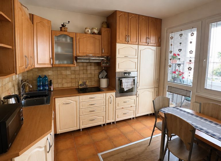 A kitchen in a 3-room apartment with light furniture and a wooden decor floor.