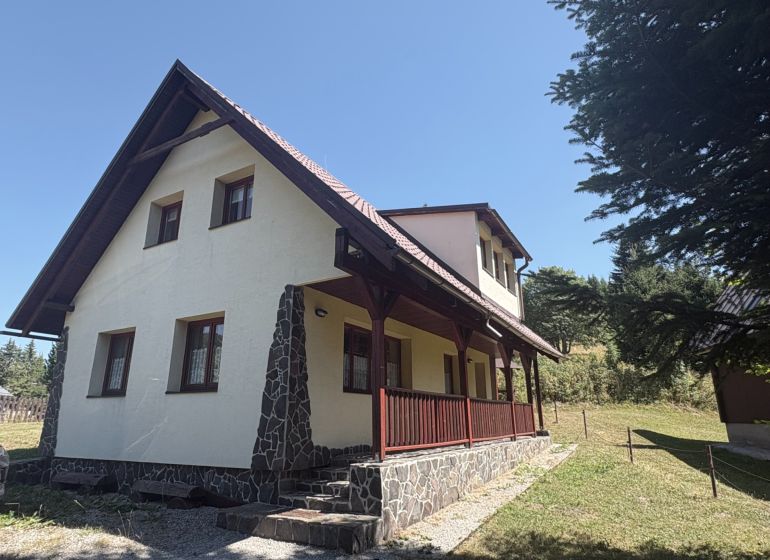 A cottage in Donovaly with a slanted roof and stone details on a sunny meadow.