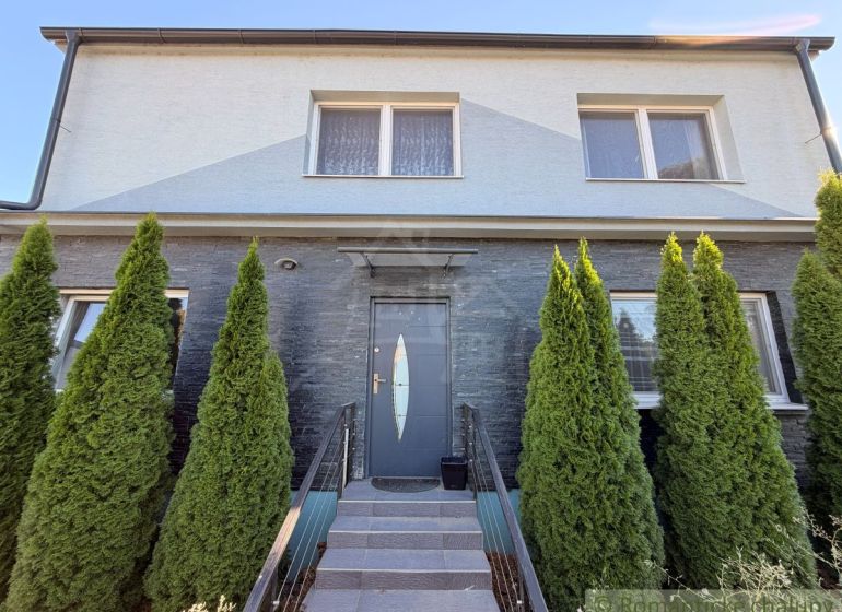 A family house in Komárno with a gray facade and thuja trees in front of the entrance.
