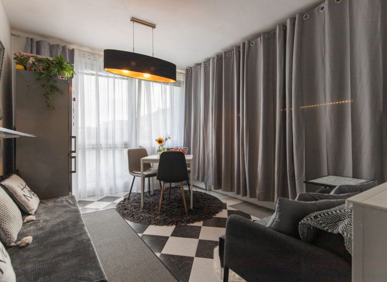 Living room in a two-room apartment with a dining table and gray curtains.