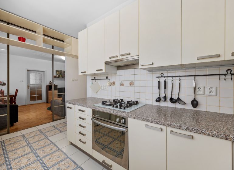 A kitchen in a 2-room apartment with a gas stove, a mirrored wardrobe, and tiles.