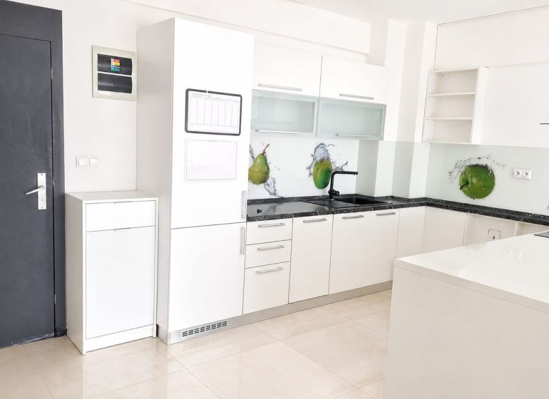 Seamless kitchen in a 2-room apartment with white cabinets and green fruit decor.