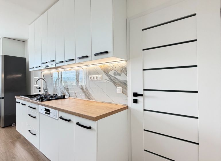 A kitchen in a studio apartment with white cabinets, marble tiles, and a wood-patterned floor.