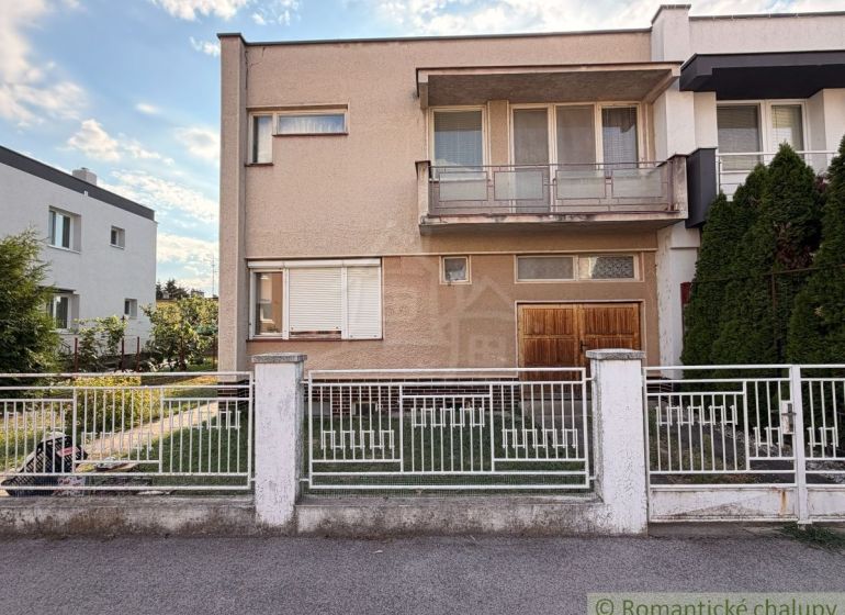 A family house in Nové Zámky with a balcony and a garden, enclosed by a white fence.