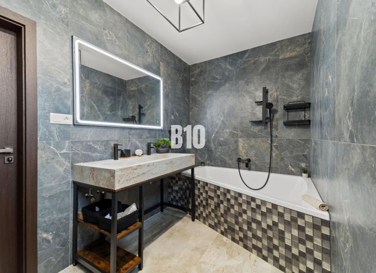 A bathroom in a family house with a bathtub, stone tiles, and a large mirror.