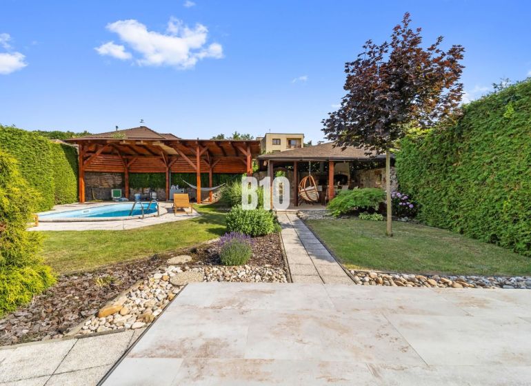 A garden of a family house in Nitra with a swimming pool and a gazebo surrounded by greenery.