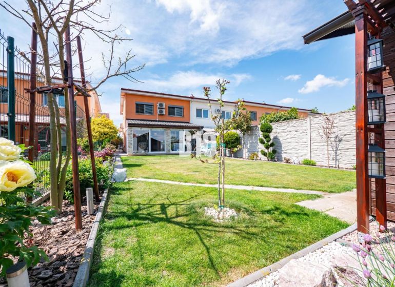 A garden at a family house in Nitra with a lawn, flowers, and a terrace.