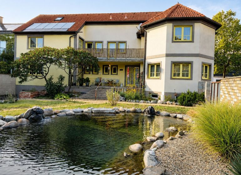 A family house in Podersdorf am See with a large garden, a pond, and solar panels.