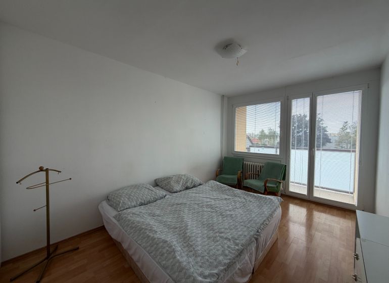 A bedroom in a 3-room apartment with a wooden decor floor, a bed, and chairs.