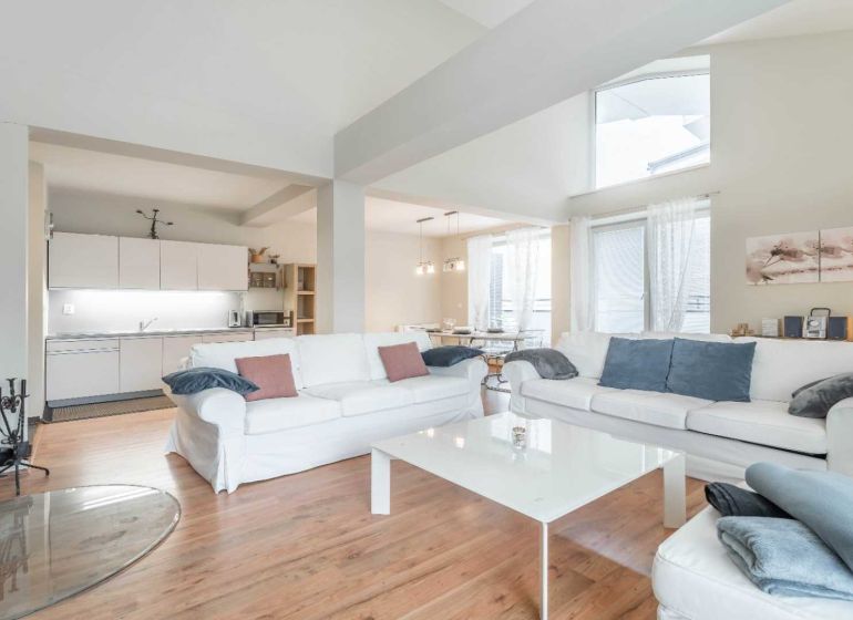 Bright living space with a fireplace, sofas, kitchen, and wood-decor flooring in a vacation apartment.