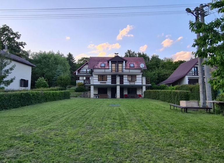 A cottage in Kaluža surrounded by greenery, maintained lawn, surroundings with trees, blue sky.