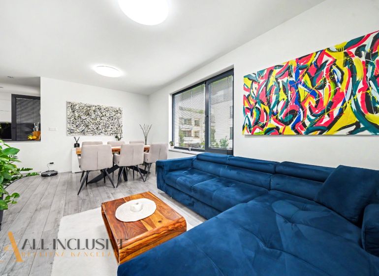 Living room of a three-room apartment with colorful paintings, a blue sofa, and a dining table.