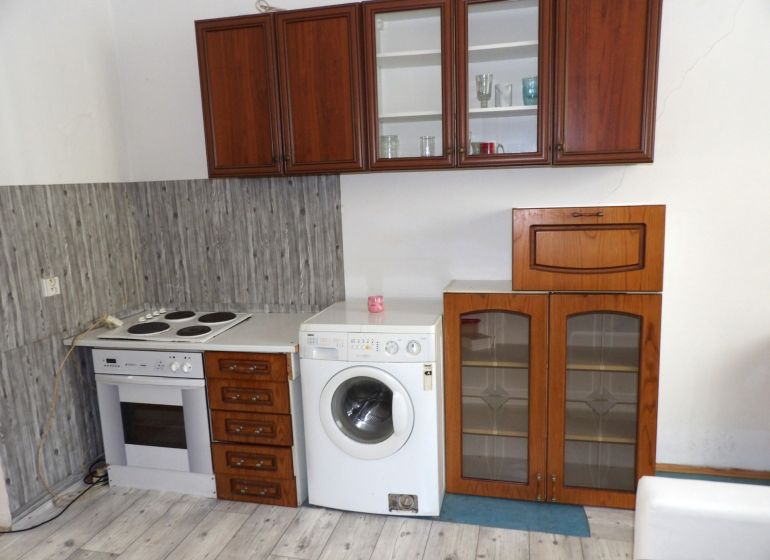 A kitchen in a 2-room apartment with an electric oven, washing machine, and a floor with a wooden decor.