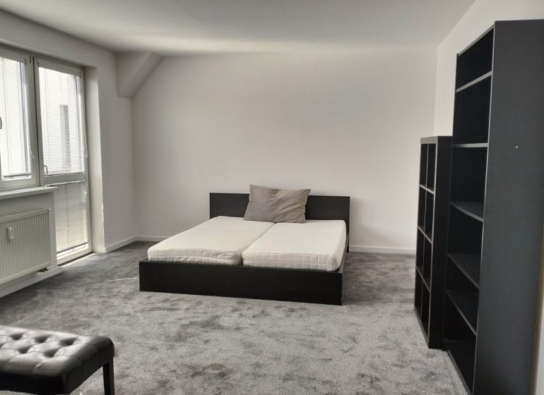 Bedroom in a 2-room apartment with a bed, shelves, and a carpet in neutral colors.