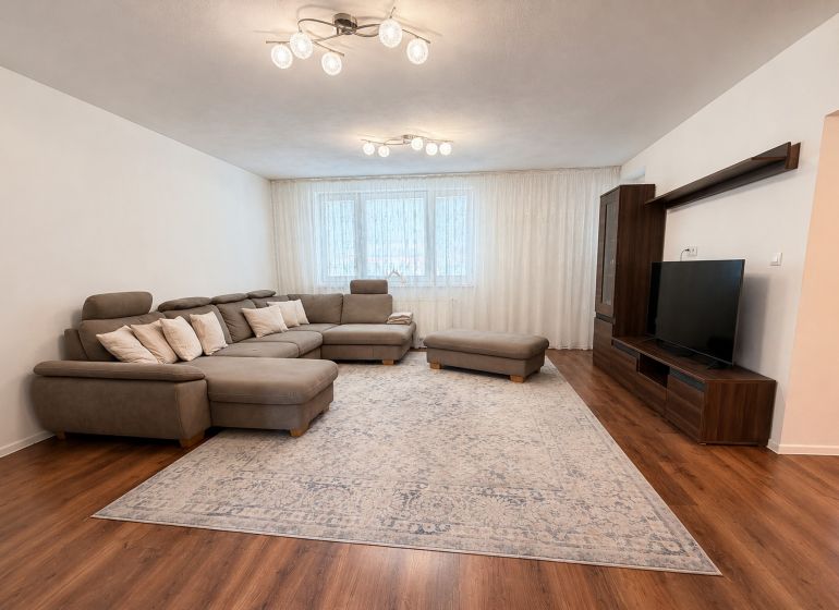 Living room with a large sofa, television, and wooden decor flooring in a family house.