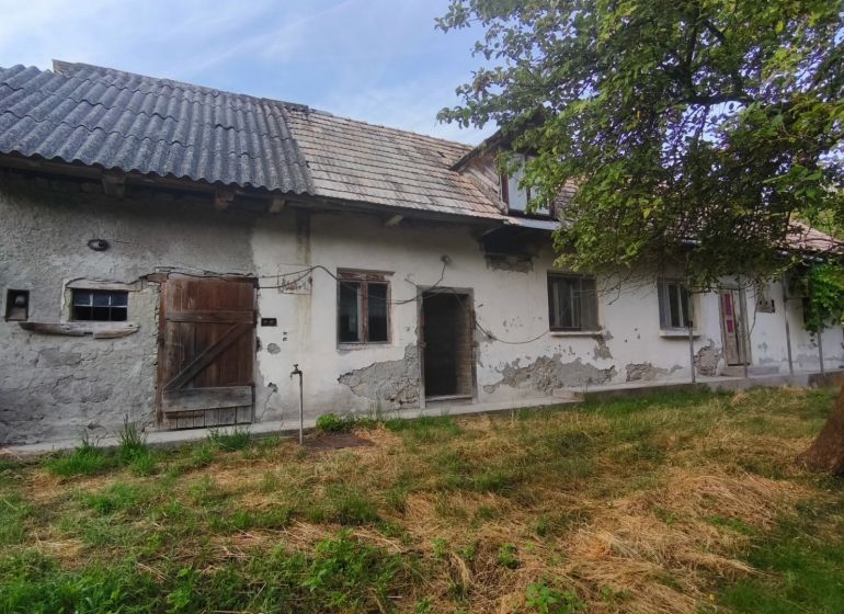 A family house in Čelovce with worn-out plaster, wooden doors, and a garden.