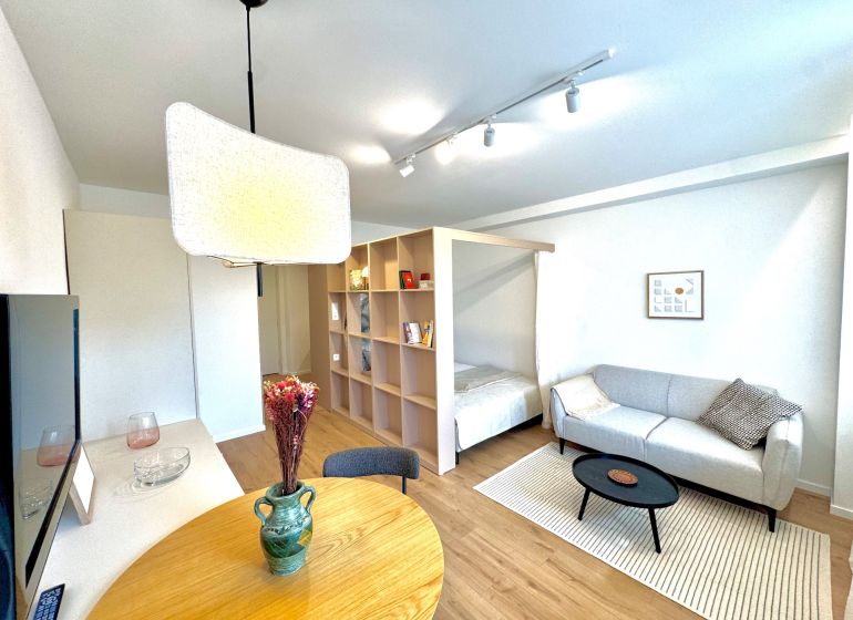 Living room with wood-patterned flooring, light-colored sofa, and dining table in a studio apartment.