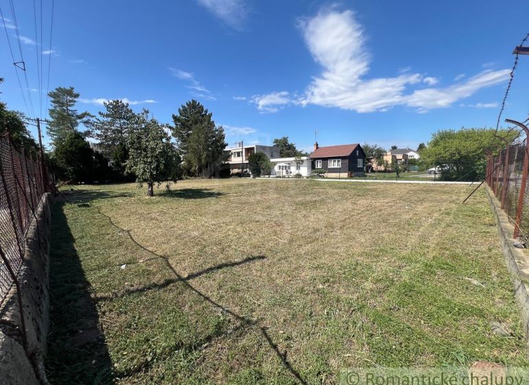 A flat plot of land in Bernolákovo with a grassy area surrounded by trees and fencing.