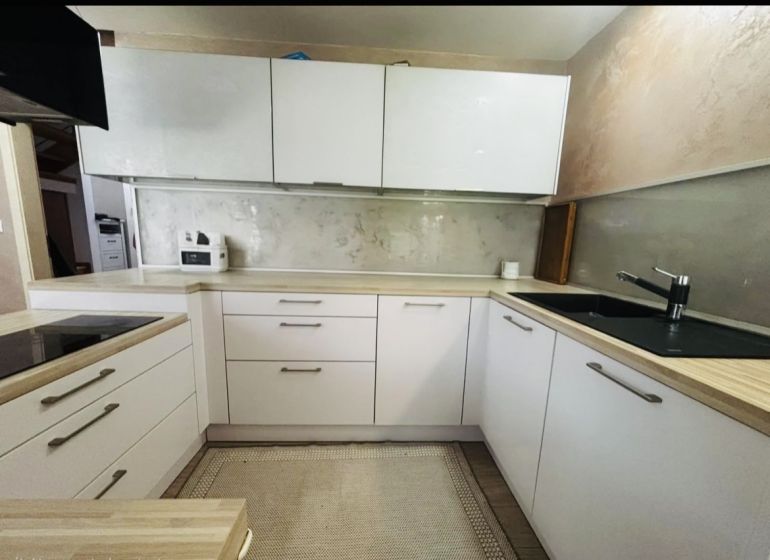 A kitchen in a 3-room apartment with white cabinets and a wooden decor countertop.