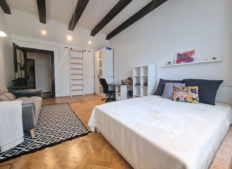A room with a bed, a sofa, and a floor with a wooden decor in a three-room apartment.