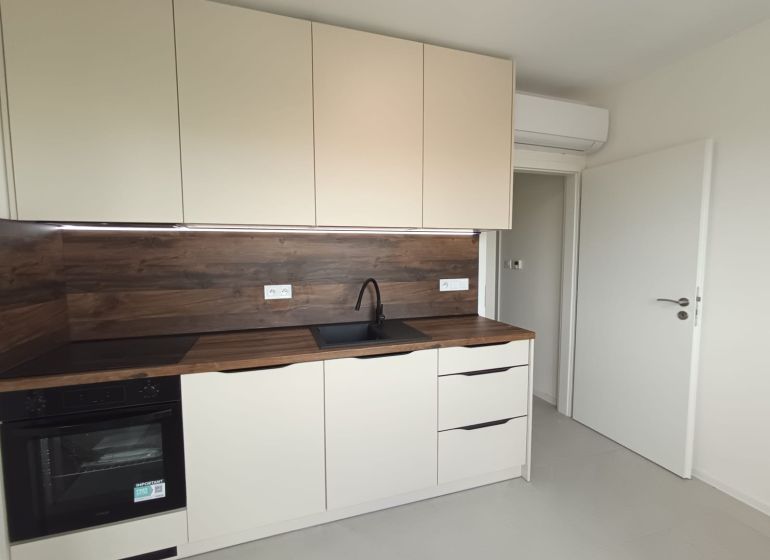 A kitchen in a 2-room apartment with white cabinets and a wood-patterned floor.