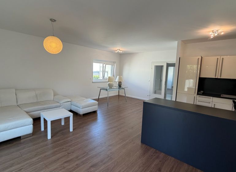 Living room in a three-room apartment with a white sofa and a wooden decor floor.