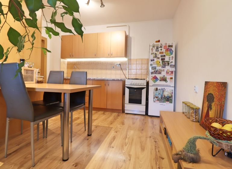 A kitchen in a 2-room apartment with a wooden decor floor, a dining table, and a refrigerator.