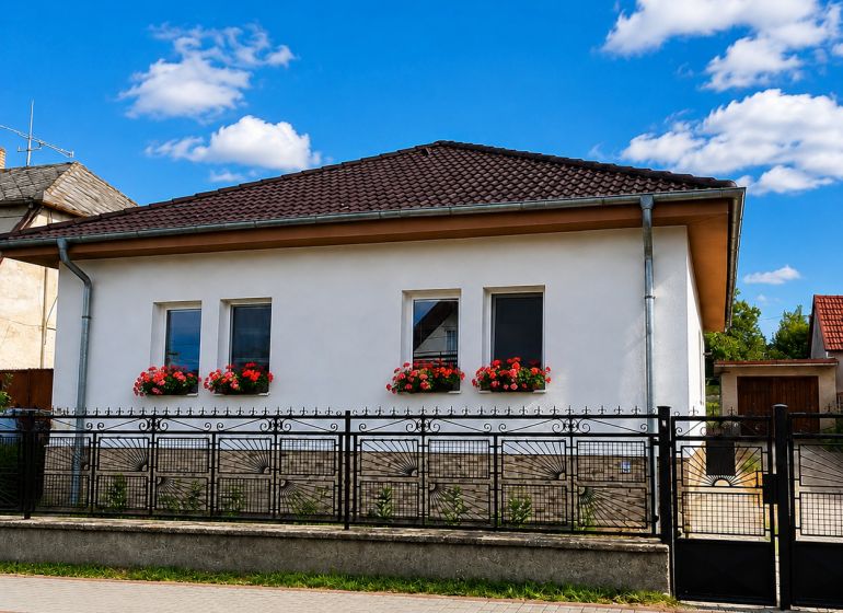 A family house in Šalgočka with a white facade, window flowers, and a hipped roof.