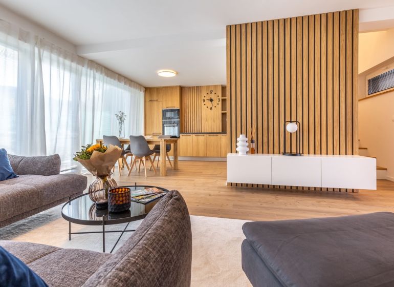 Living room in a family house with wood-patterned flooring and a dining area in the background.