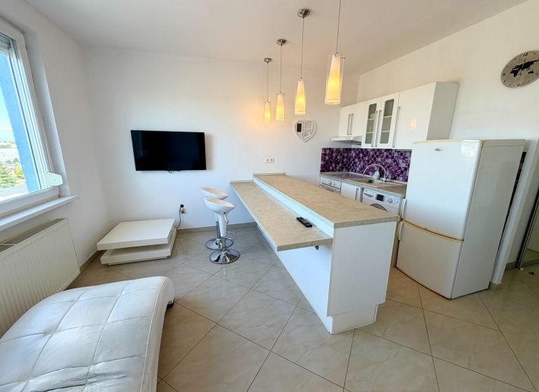 A kitchen in a studio apartment with bar stools and purple wall tiles.