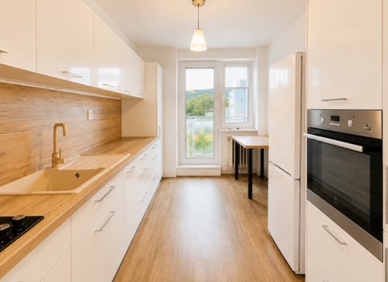 A kitchen in a 3-room apartment with a wooden decor floor, white cabinets, and a stove.