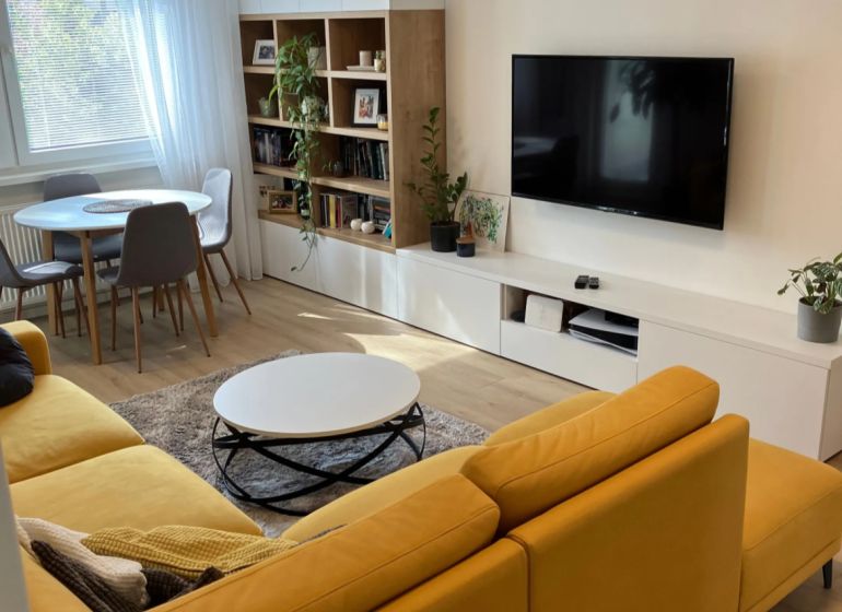 Living room in a 3-room apartment with a comfortable sofa, dining table, and wooden decor flooring.
