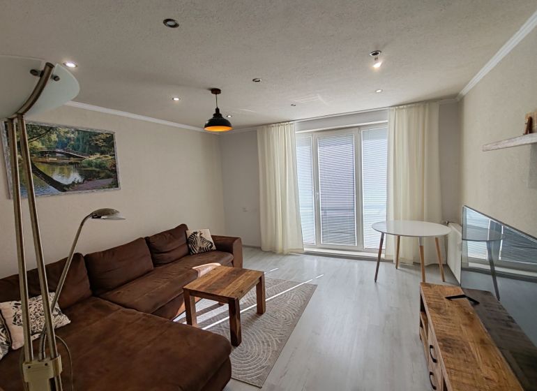 A living room in a three-room apartment with a wooden decor floor and a brown sofa.