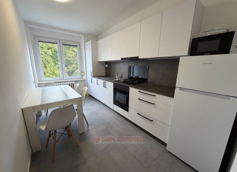 The kitchen in a 2-room apartment with a light dining table and white cabinets.